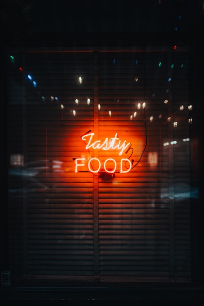 A vertical shot of bright neon lights spelling "Tasty Food"