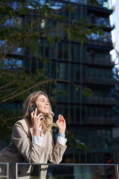 Vertical shot of businesswoman on a call standing outside business center talking on mobile phone