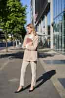 Free photo vertical shot of businesswoman walking on street with digital tablet going to work wearing beige sui