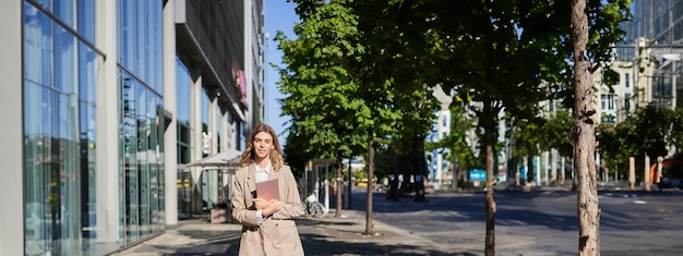 Free Photo vertical shot of businesswoman walking on street with digital tablet going to work wearing beige