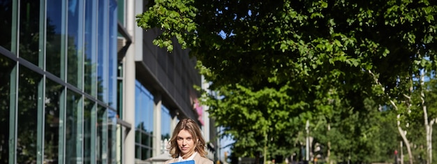 Free Photo vertical shot of businesswoman with folder standing on a street near office buildings wearing suit