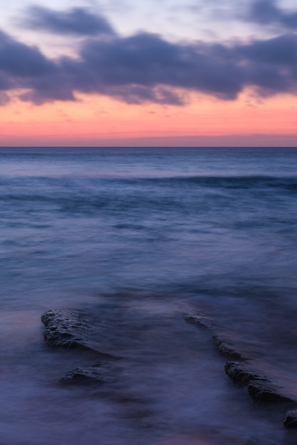 Free photo vertical shot of a calm ocean with small waves and an orange cloudy sky