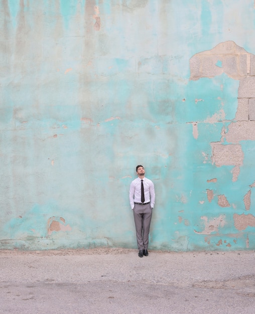 Free photo vertical shot of a caucasian male wearing a shirt and tie while standing in front of a green wall