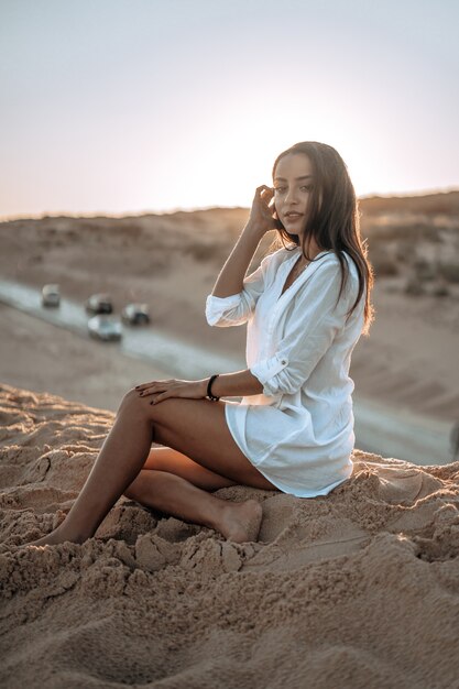 Vertical shot of a Caucasian woman in a white dress posing on the beach