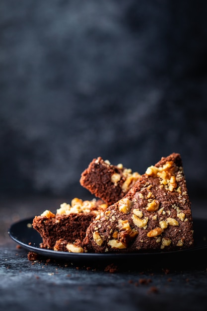 Vertical shot of a chocolate cake with walnuts in a black plate with a blurred