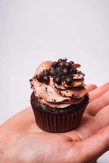 Vertical shot of a chocolate cupcake on man's hand on a white background