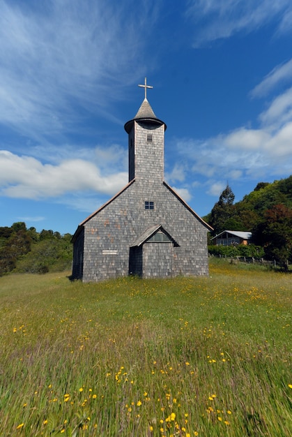 Vertical shot of a church in a grassy field under a blue sky