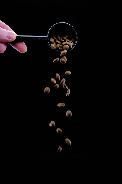 Free photo vertical shot of coffee beans dropping from a coffee scoop isolated on black