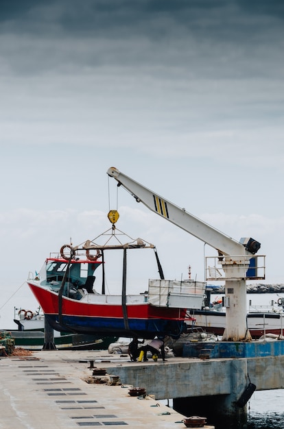 Free Photo vertical shot of a crane lifting a white boat on a pier