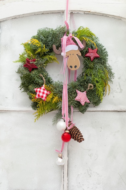 Free photo vertical shot of a decorative christmas wreath with ornaments hanging on a white door