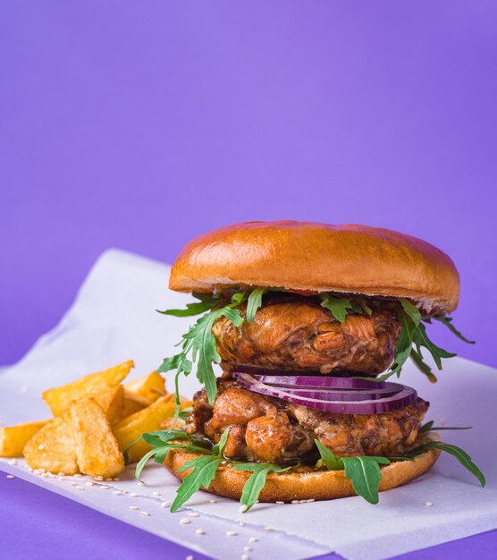 Vertical shot of a delicious burger with chicken onions and rocket served with fried potatoes