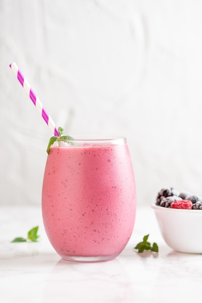 Vertical shot of a delicious mix berry milkshake with different berries in a bowl next to it