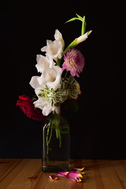 Vertical shot of different flowers in a jar on a wooden surface with a black background