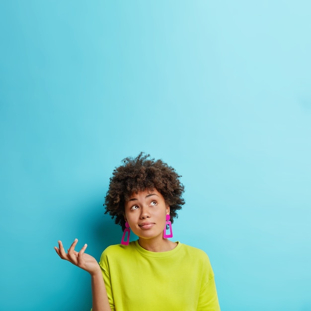 Free Photo vertical shot of doubtful afro american woman raises hand with doubt looks confused above makes decision