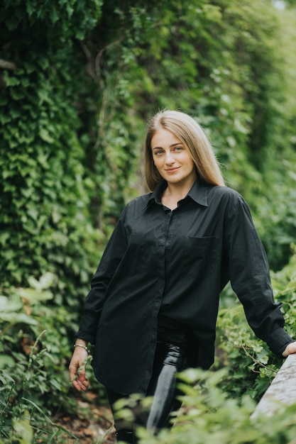 Vertical shot of a fashionable caucasian blonde female posing surrounded by greenery