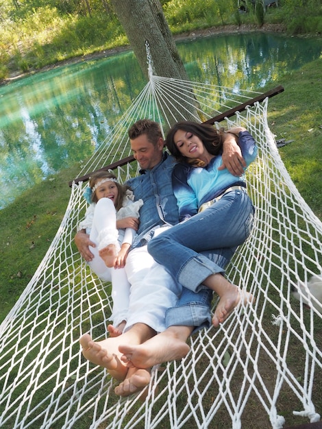 Free photo vertical shot of the father, mother and their daughter lying on the hammock in the garden