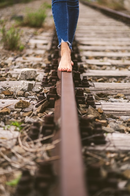 Free Photo vertical shot of a female in jeans walking through the train rails barefoot