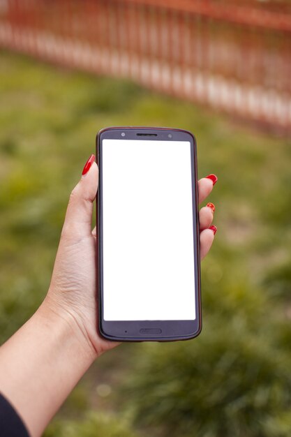 Vertical shot of a female with red nail polish holding a phone with a blank screen