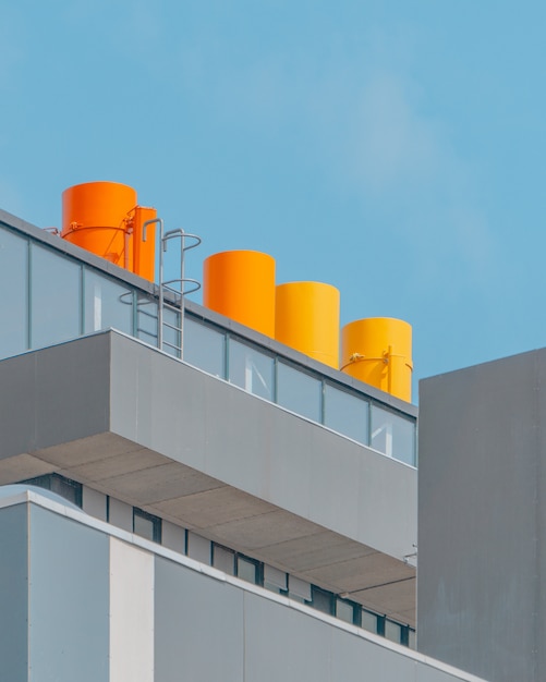 Free photo vertical shot of a glass building with orange chimneys under the blue sky