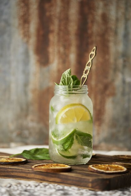 Vertical shot of a glass jar mojito drink with mint leaves and lemon slices on a wooden drink