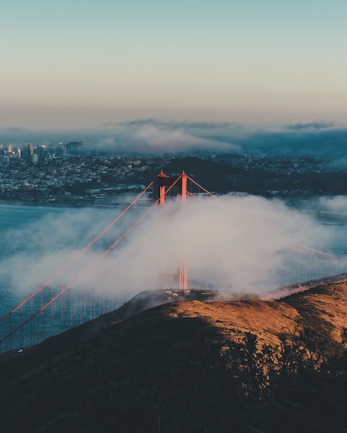 Free photo vertical shot of the golden gate bridge behind the clouds with buildings in the distance