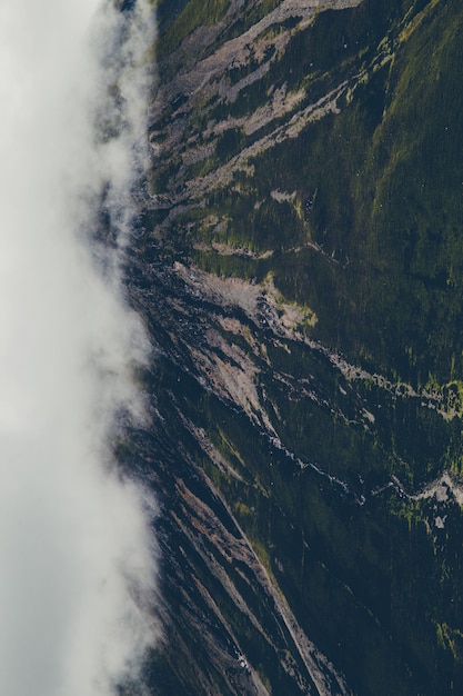 Vertical shot of green mountains covered with white clouds