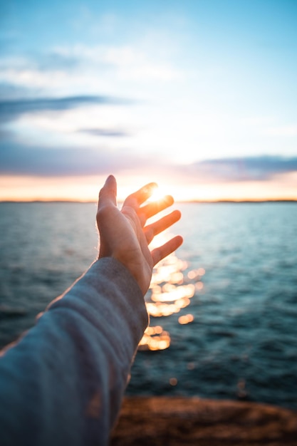 Vertical shot of a hand with the beautiful sea in the background during suns