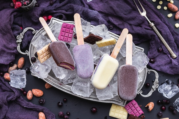 Free photo vertical shot of home-made vegan icecreams and chocolate bars on ice cubes in a metal plate