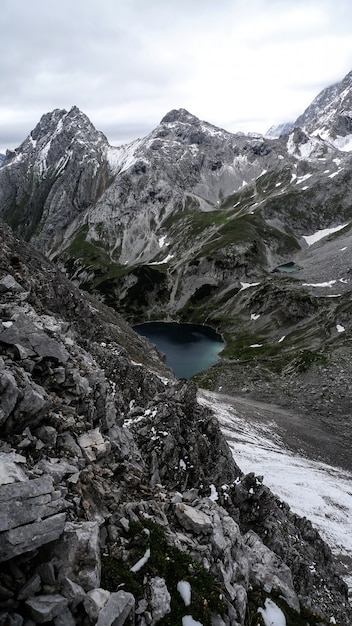 Vertical shot of a lake surrounded by mountains under a cloudy sky