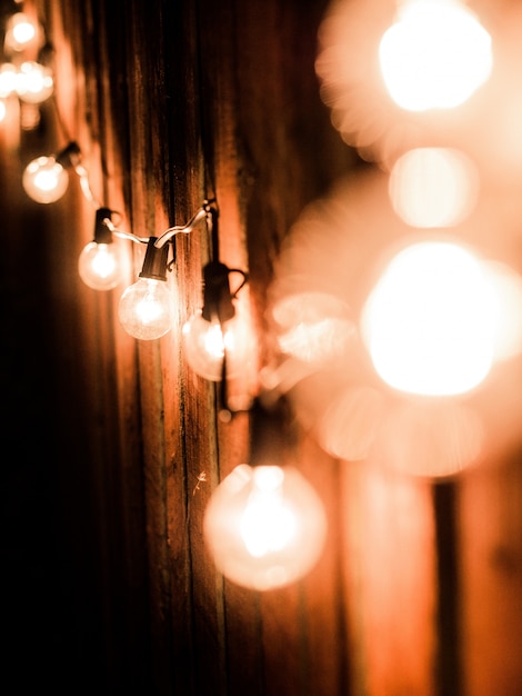 Vertical shot of lit lightbulbs on an electrical wire near a wooden fence