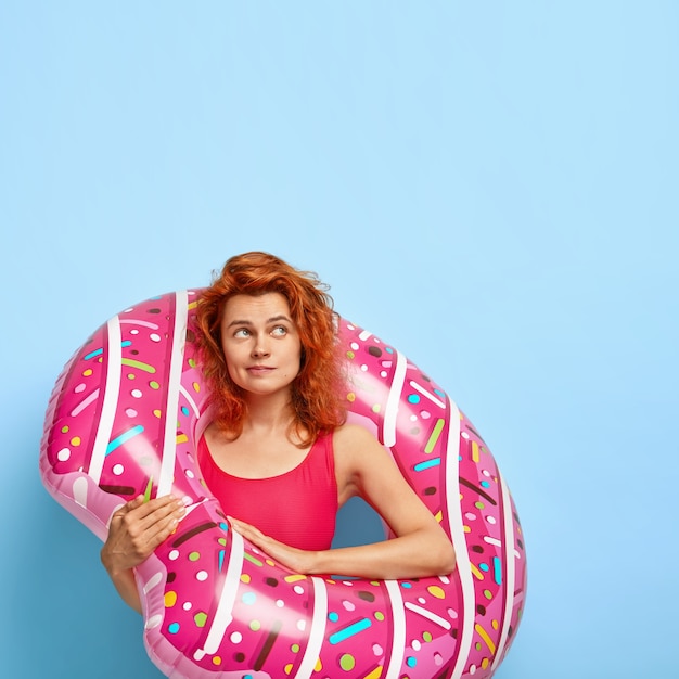 Free Photo vertical shot of lovely red haired woman with dimples on cheeks, focused aside, plans future vacation