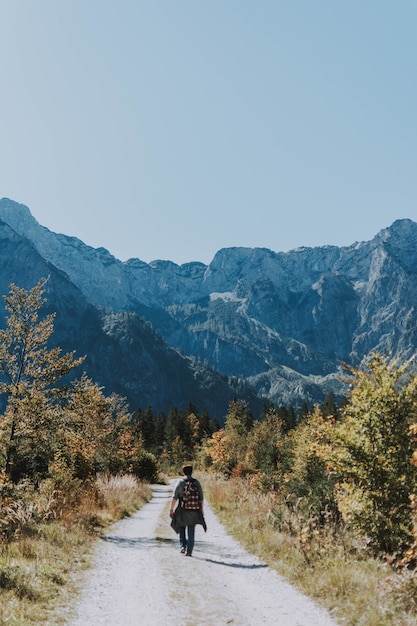 Free photo vertical shot of a male hiker venturing through a narrow gravel road towards rocky mountains