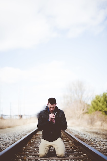 Free photo vertical shot of a male on his knees on train tracks and praying while his eyes are closed