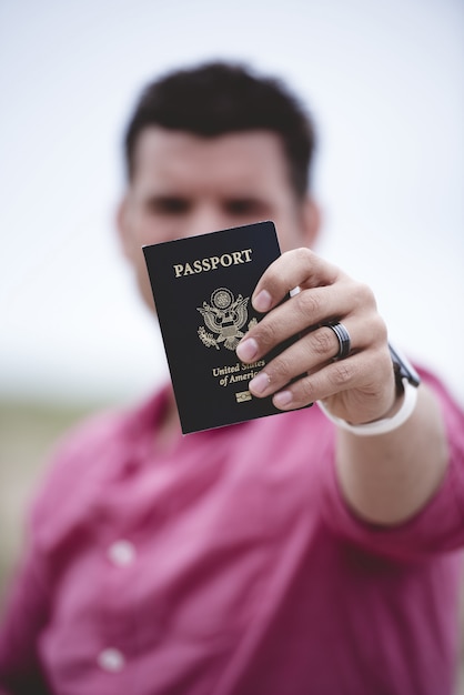 Free photo vertical shot of a male holding up his passport towards the camera with a blurred background