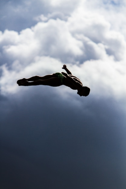 Free Photo vertical shot of a male jumping into the air with a blurred sky