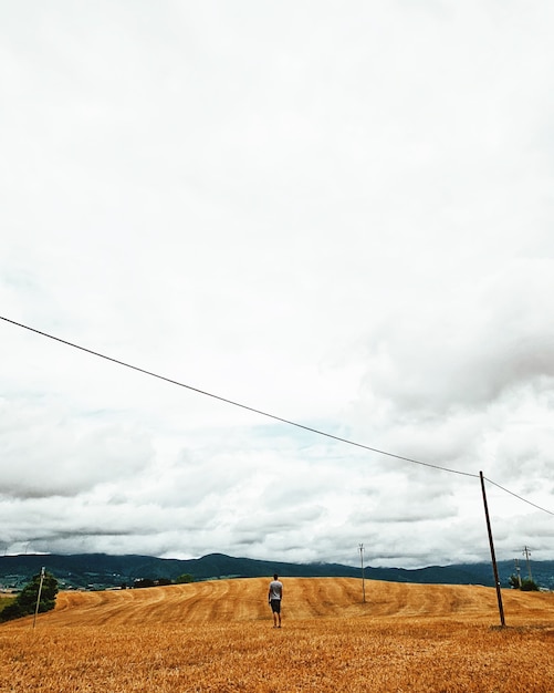 Vertical shot of a male standing in an empty field under a cloudy sky