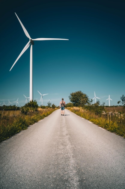 Free Photo vertical shot of a man walking on the road with windmill turbines on the roadsid