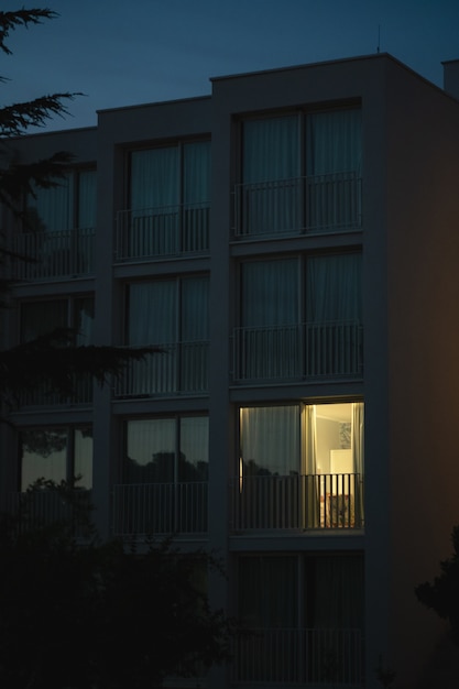 Free Photo vertical shot of a modern white building with light coming out from one of the big balcony windows