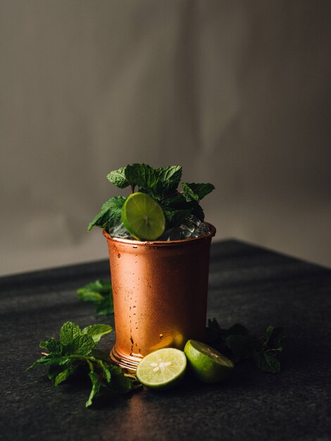 Vertical shot of a mojito cocktail I a copper cup with lemon and mint leaves around it