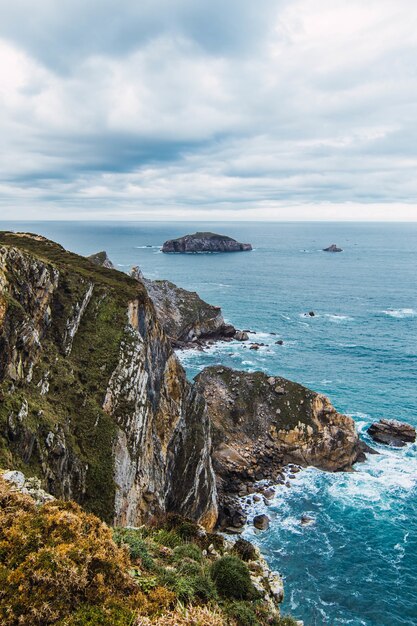 Vertical shot of the mountains near the sea under a cloudy sky in Cabo Penas, Asturias, Spain