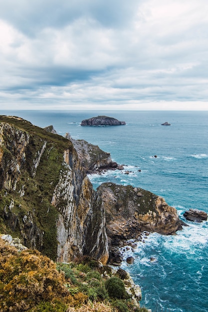 Vertical shot of the mountains near the sea under a cloudy sky in Cabo Penas, Asturias, Spain