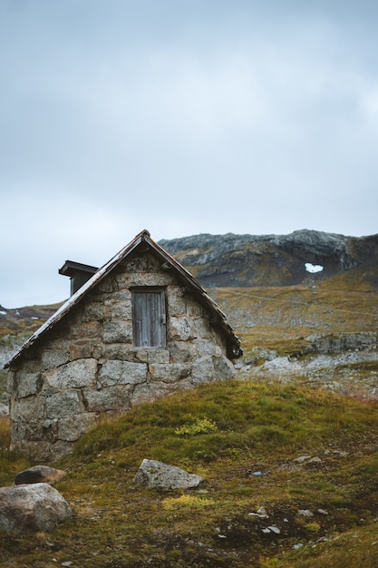 Free photo vertical shot of an old abandoned cabin in a grassy field in finse, norway