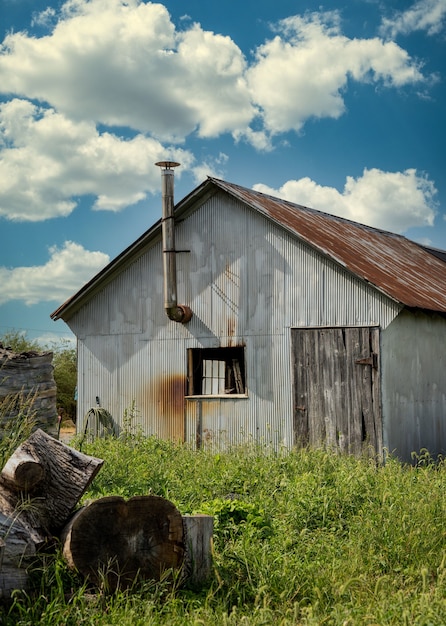 Free photo vertical shot of an old barn in a field with a weathered roof under a cloudy sky