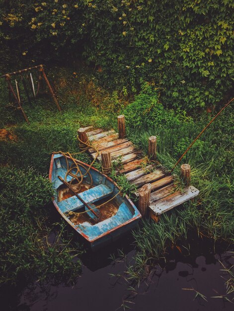 Vertical shot of an old boat in the water near a wooden dock surrounded by greenery