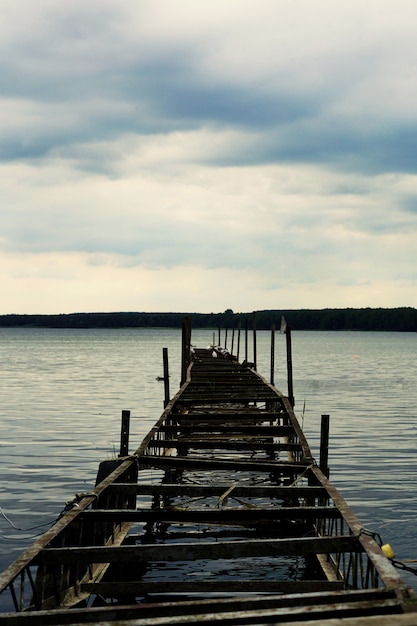 Free photo vertical shot of an old half-broken pier with cloudy skies in miedwie, stargard, poland.