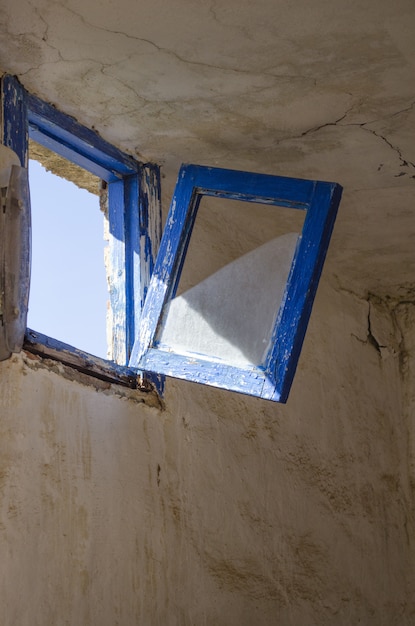 Free photo vertical shot of an old rustic blue window about to break and fall in the dilapidated room