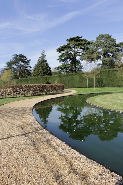 Vertical shot of a path in a green park with trees and a lake under the blue sky