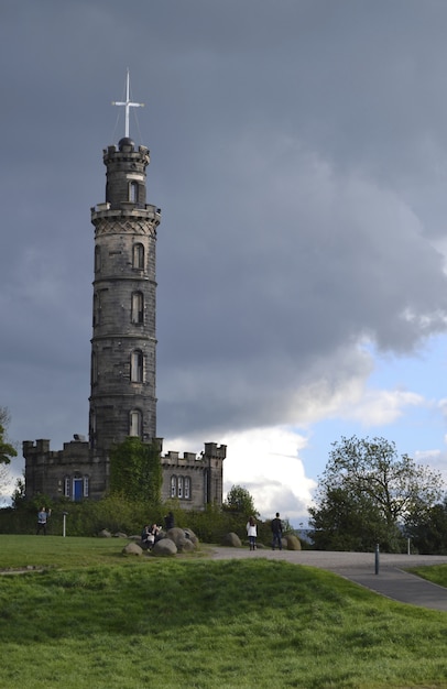 Free photo vertical shot of a pathway with people walking near a grassy field and a tower under a cloudy sky