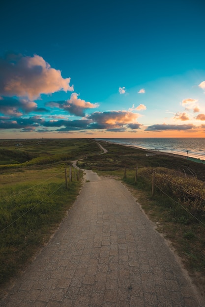 Free photo vertical shot of a paved pathway by the sea under the cloudy sky captured in domburg, netherlands