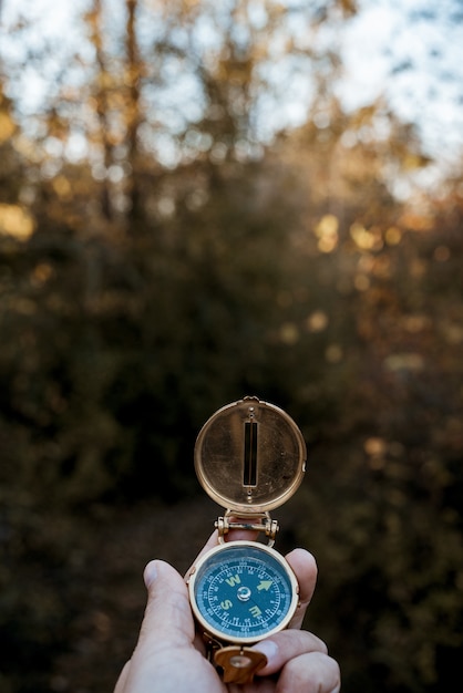 Free photo vertical shot of a person holding a compass with a blurred natural background